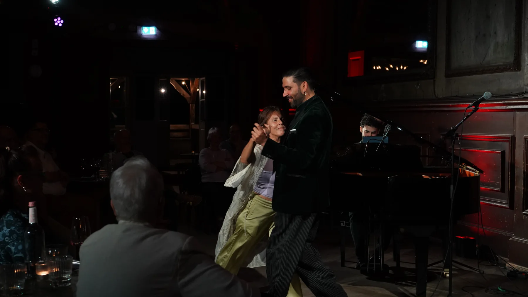 Rolando Guy dancing with a member of the audience while Gastón Efficace plays piano